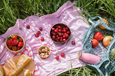 Zero waste summer picnic on the with cherries in the wooden coconut bowls, fresh bread and glass bottle of juice or smoothie on pink blanket, flatlay Picknick