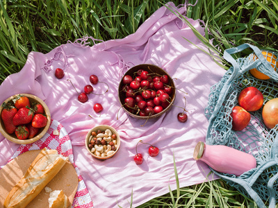 Zero waste summer picnic on the with cherries in the wooden coconut bowls, fresh bread and glass bottle of juice or smoothie on pink blanket, flatlay Picknick