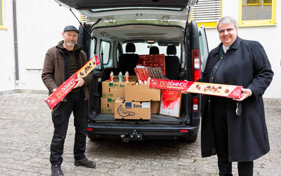 Caritas-Hausmeister Alfred Krafft und der Vorsitzende des Diözesan-Caritasverbands, Domkapitular Clemens Bieber, nehmen sich am Caritashaus die Schokoladenspende der Unternehmerfamilie Trabold in Empfang.