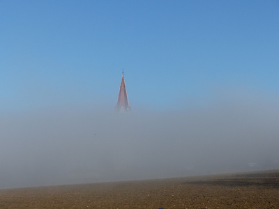 Der Nebel lichtet sich – der Blick wird weit und klar: Blick über die Felder auf die Abteikirche von St. Ottilien.