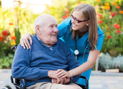 Symbolbild: Eine junge Pflegerin kümmert sich um einen älteren Herrn im Rollstuhl.